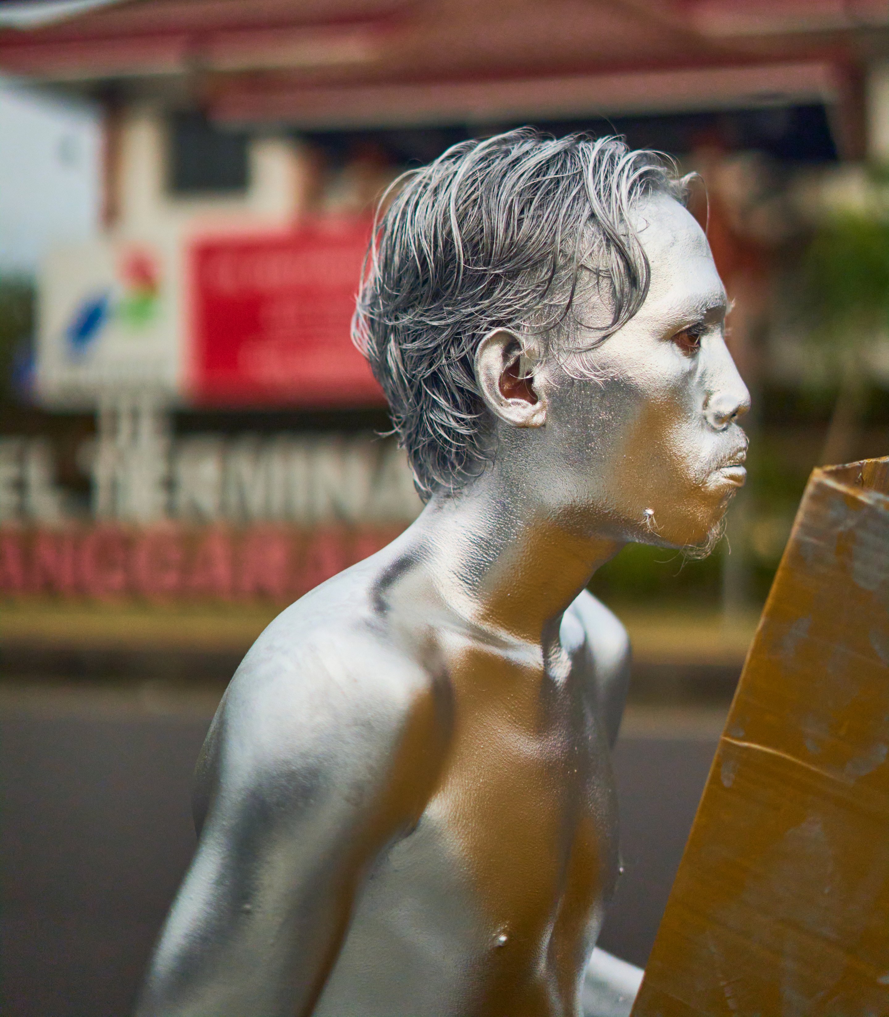 White stone sculpture of a man's head and shoulders in profile, with blurred buildings and storefront signage in the background.