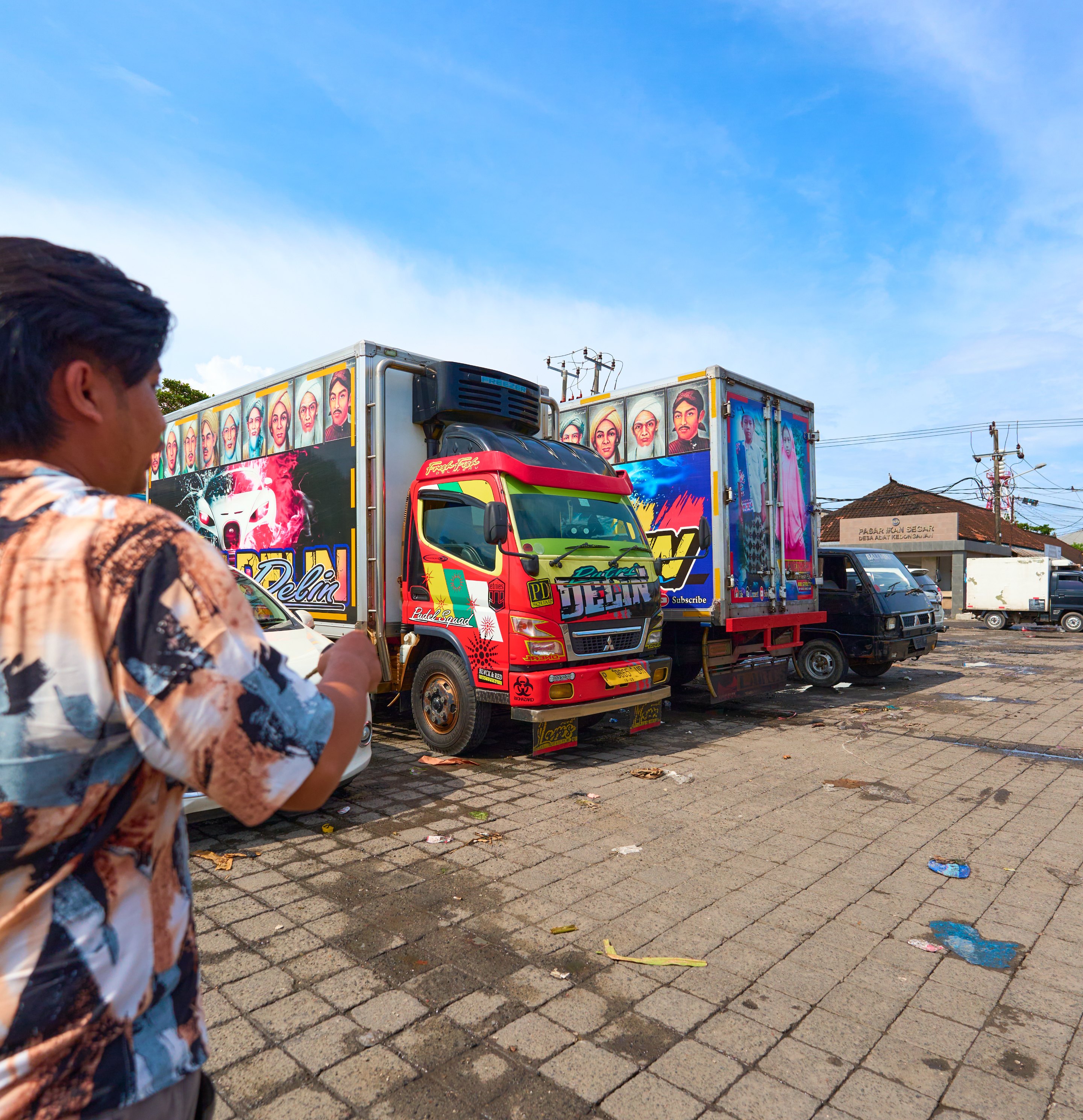 Woman looking at a decoratively painted truck covered in vibrant red and multicolored artistic designs in an urban street setting.