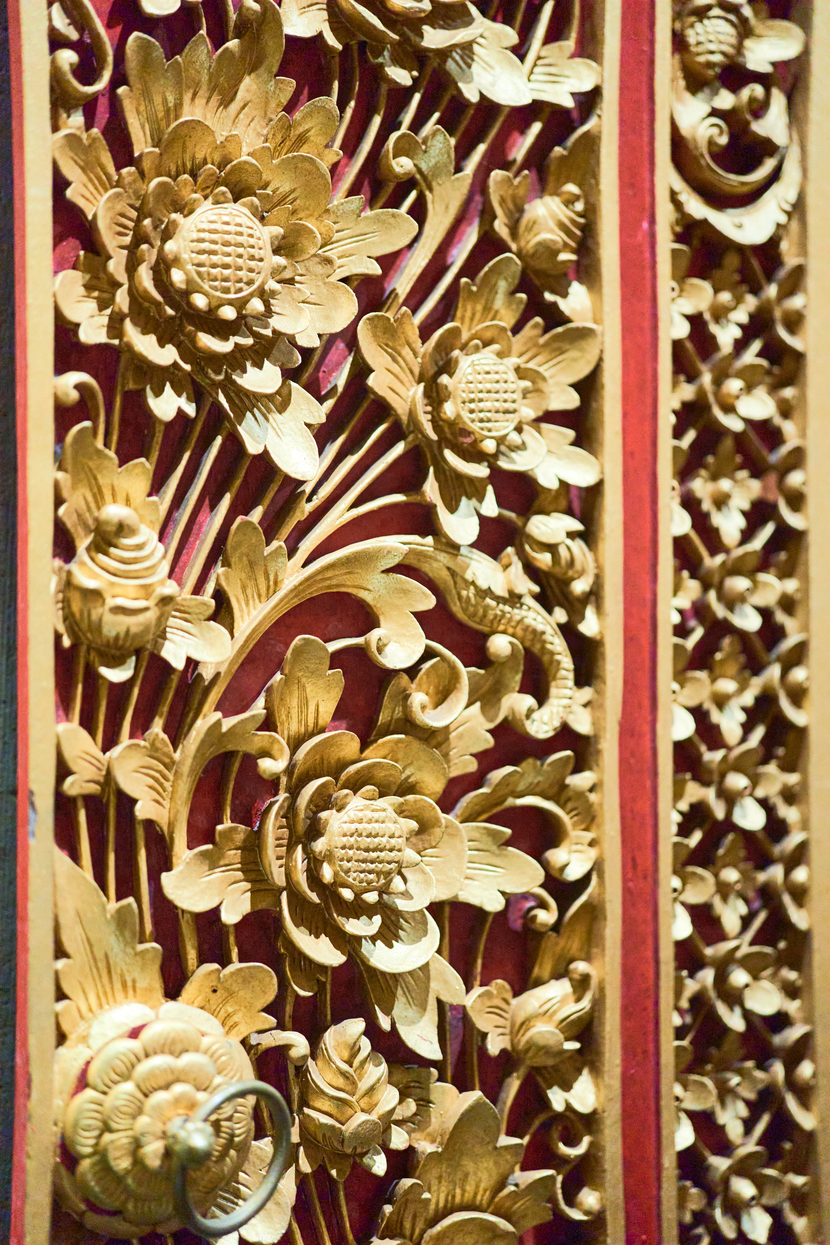 Ornate carved wooden temple decoration featuring golden floral reliefs arranged in intricate patterns against a deep red background.