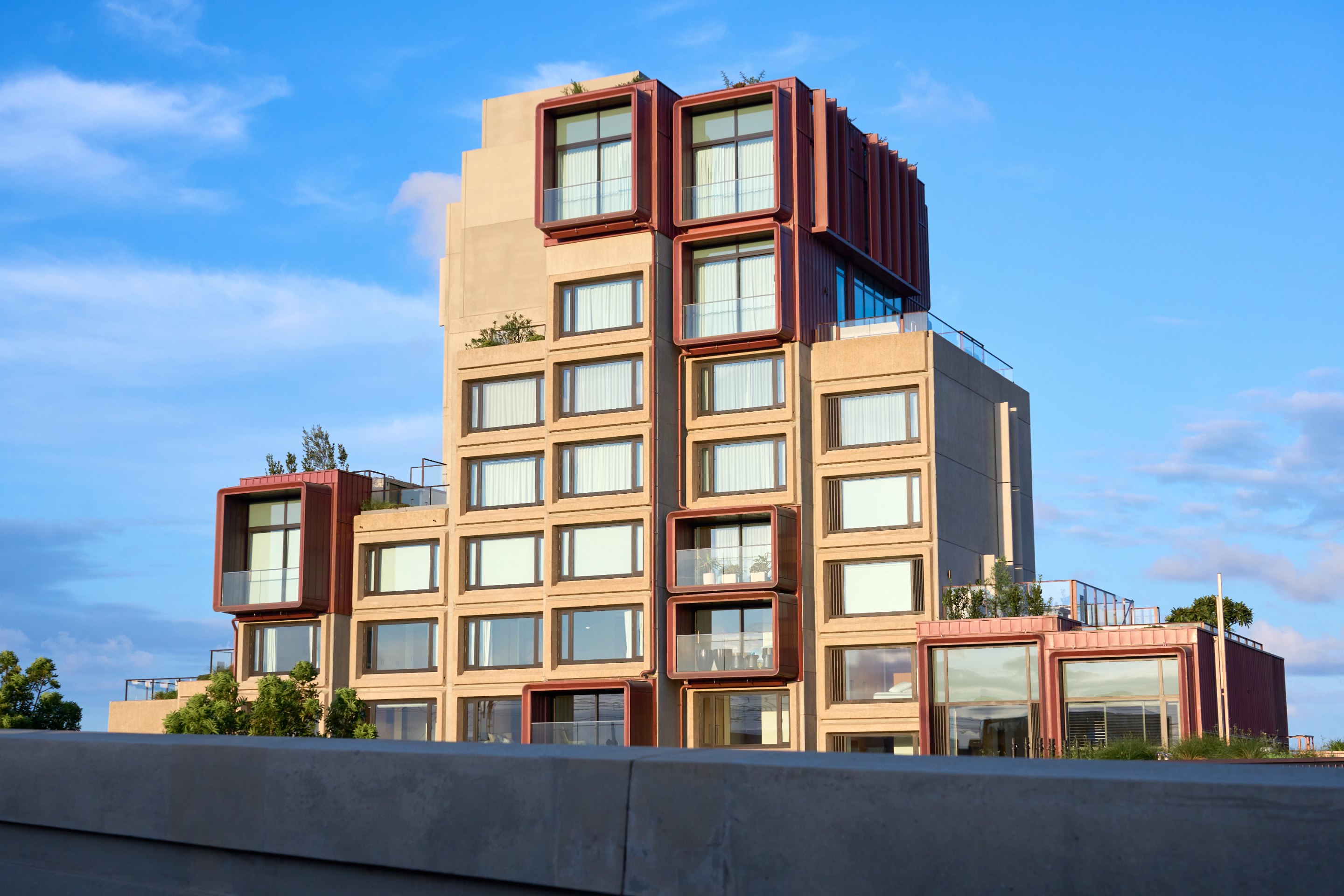 Contemporary apartment building with striking stacked window pattern creating textured facade in tan and reddish-brown brick, clear blue sky.