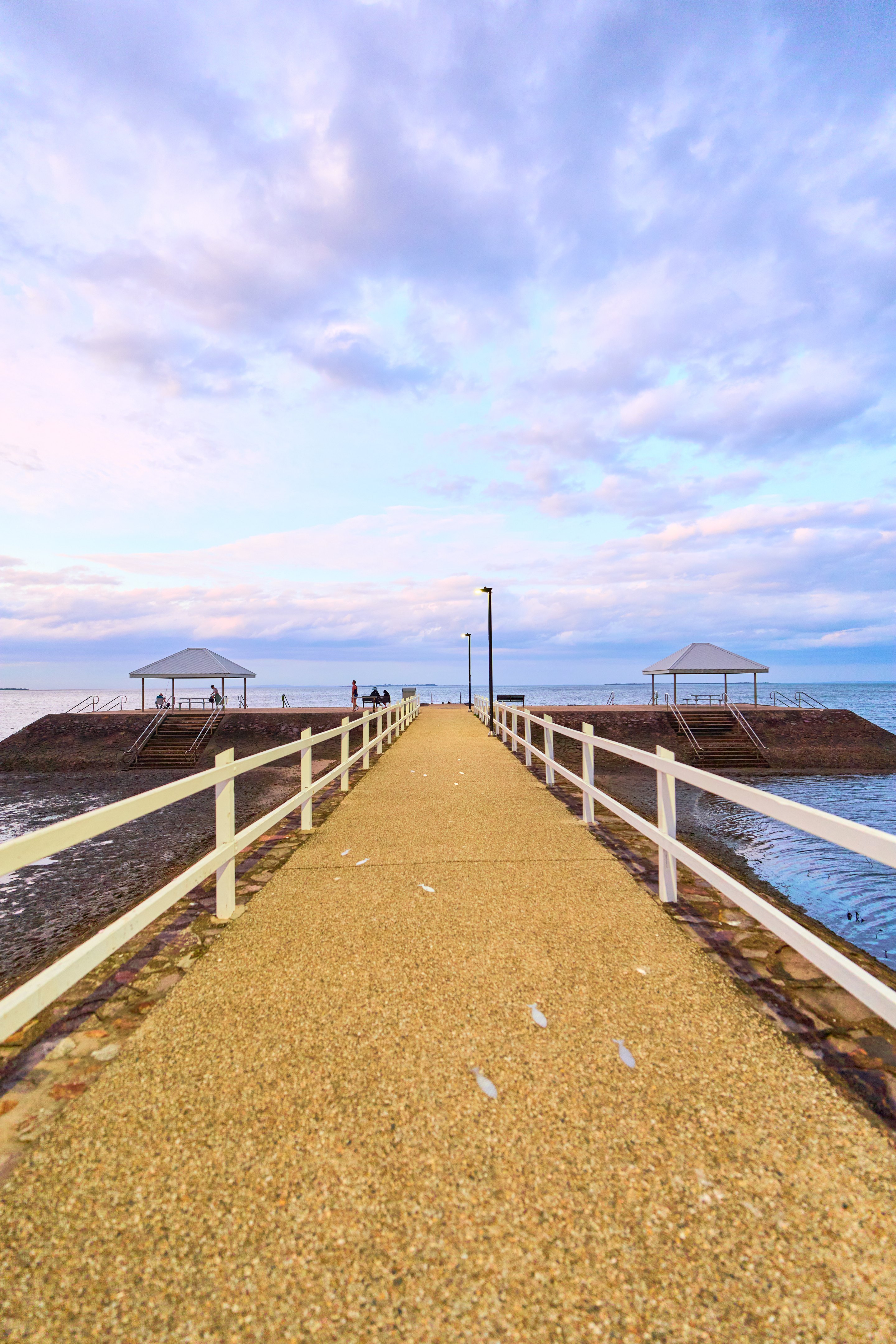 Long wooden boardwalk extending toward the horizon between still water and wetlands, with pavilion structures and white railings.