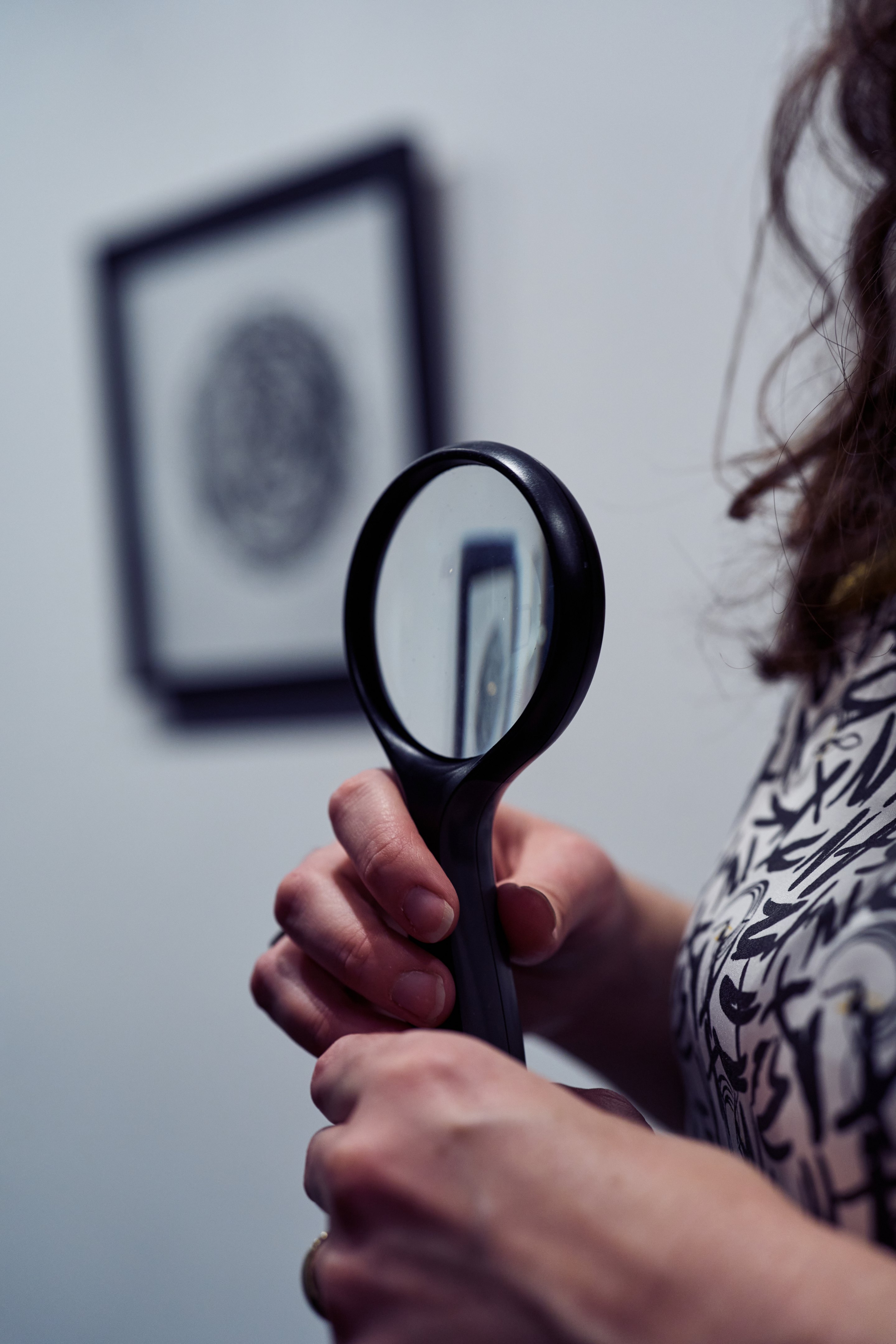 Hand holding magnifying glass with framed portrait visible through the lens and blurred in the background.