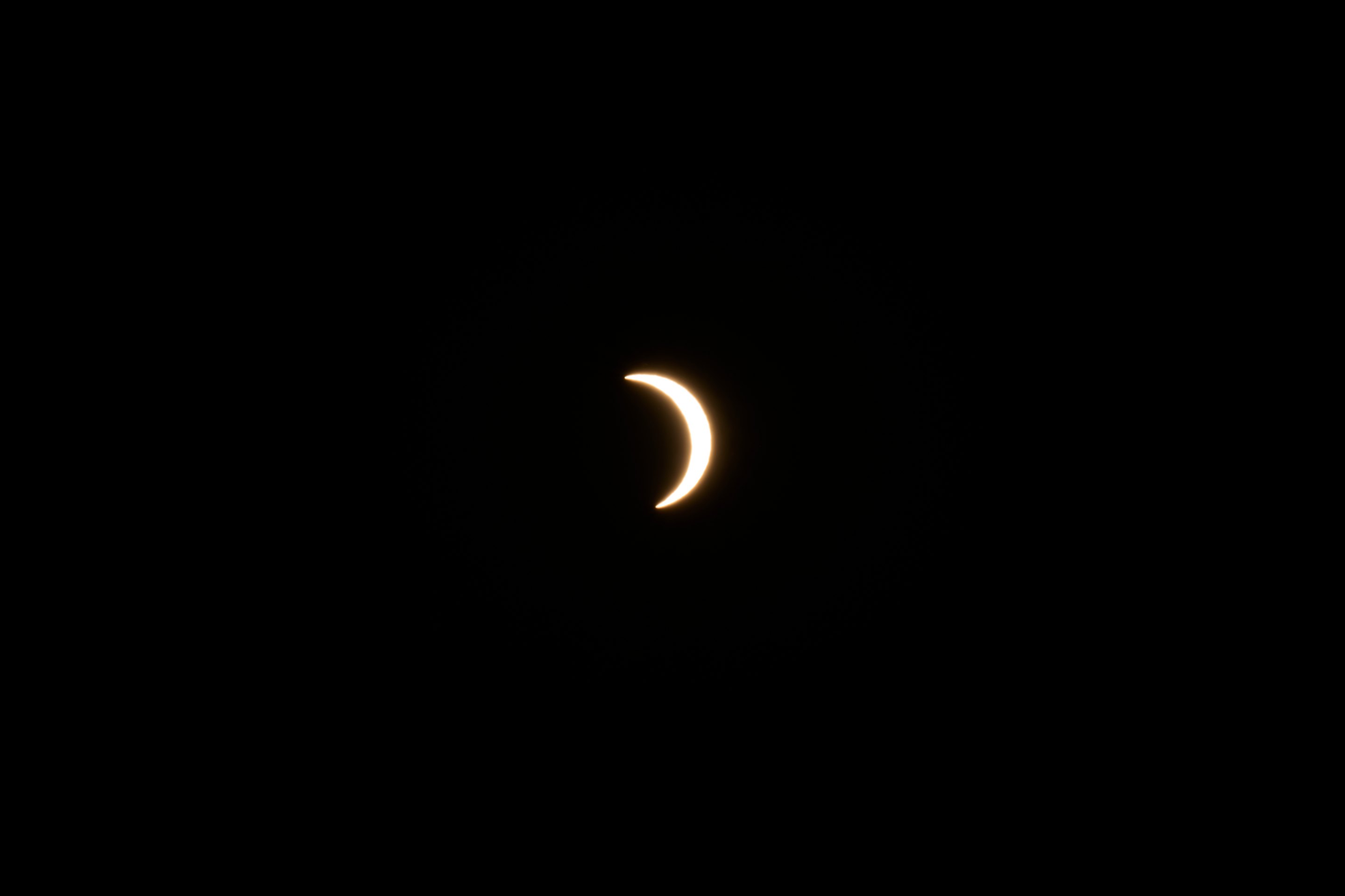 Thin crescent moon during solar eclipse glowing against black sky.