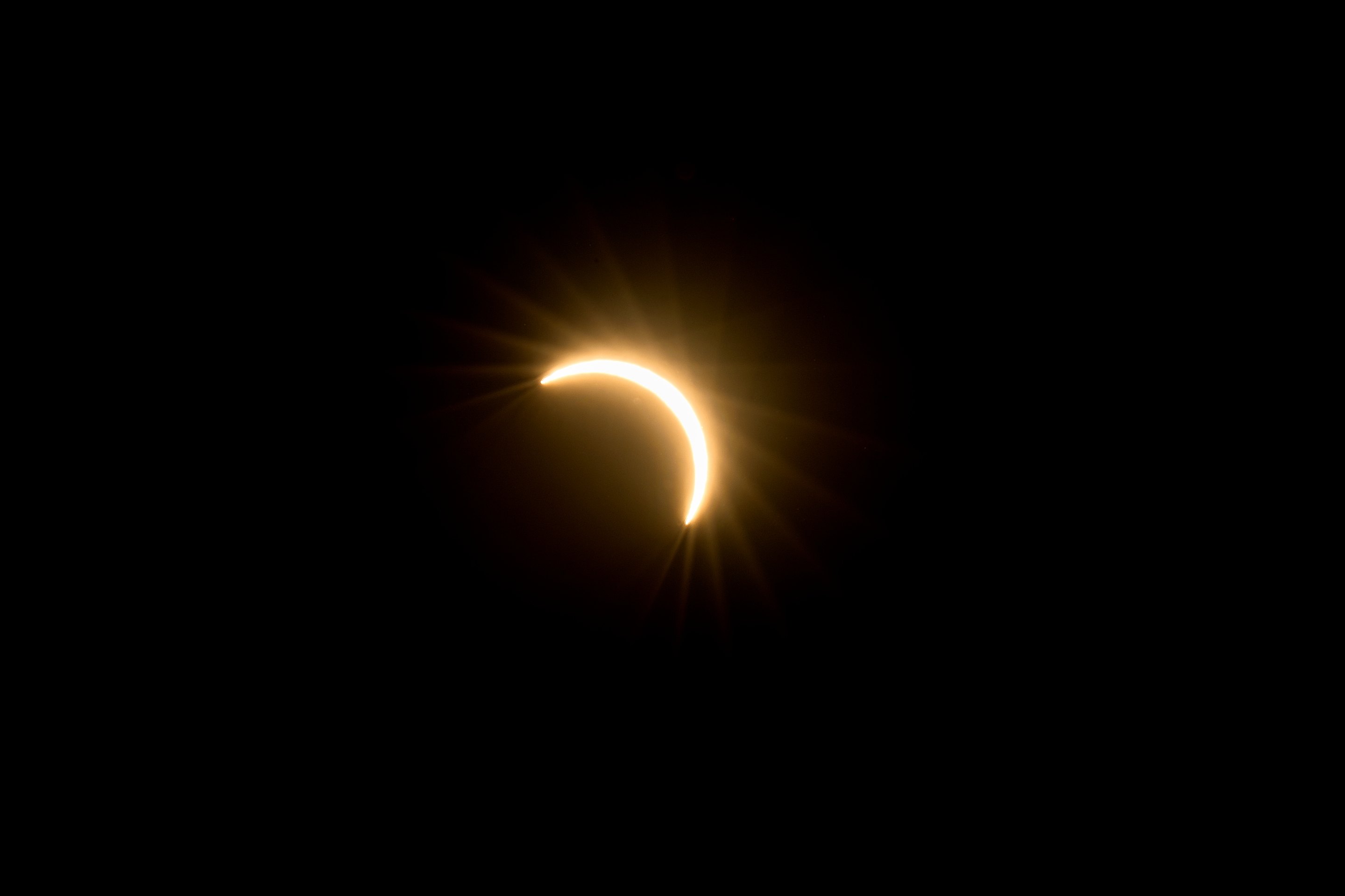 Crescent moon during solar eclipse with golden glow against dark sky.